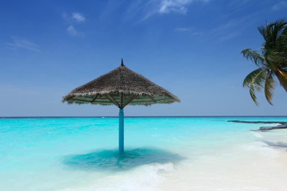 Ein Strand mit Palmen und einem strohgedeckten Sonnenschirm auf den Malediven.